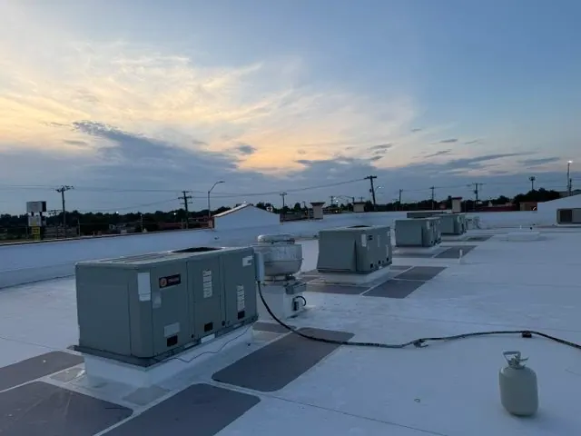 Row of Trane commercial HVAC rooftop units installed on a flat white roof at sunset